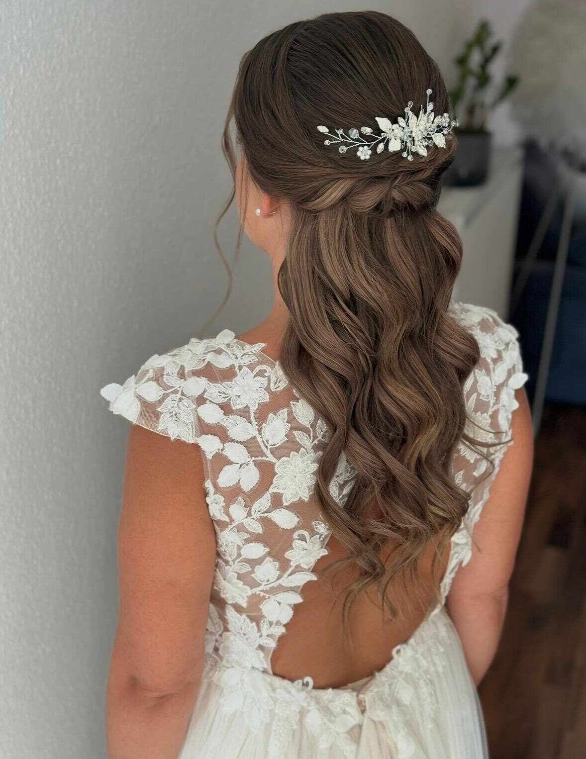 Braut von hinten mit offenen Wellen und floralem Haarschmuck in einem Spitzenkleid