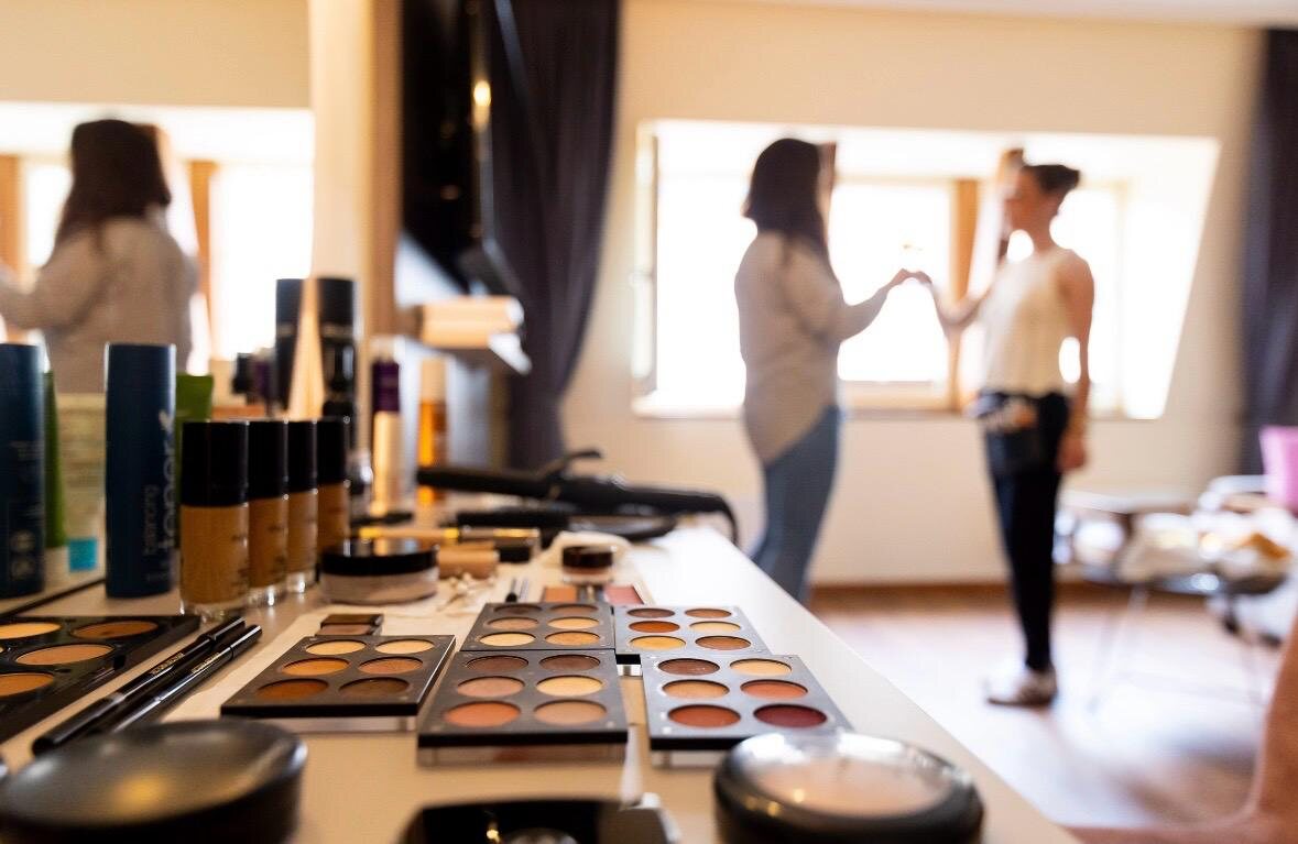 Make-up-Paletten und Pinsel im Vordergrund, Braut am Fenster im Hintergrund